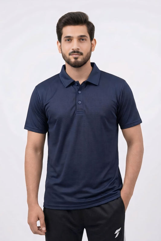 A man wearing a navy blue short-sleeve polo shirt and black track pants, standing against a light gray studio background.