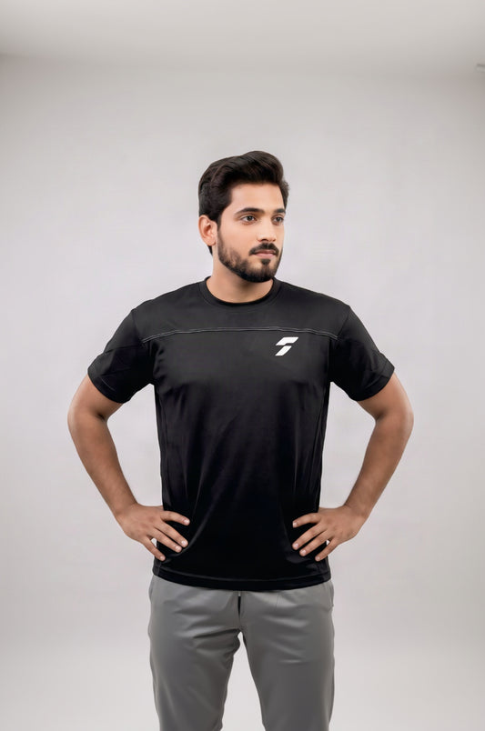 A man wearing a black athletic t-shirt with a white logo on the chest, standing with hands on hips against a light gray background.