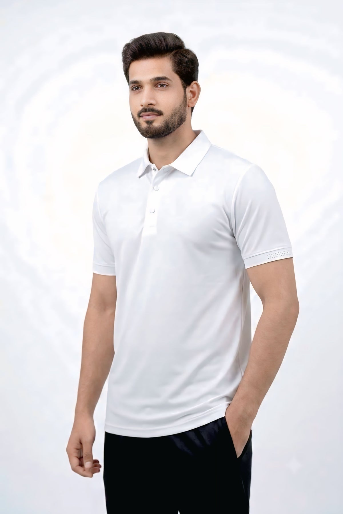A man wearing a white short-sleeve polo shirt and black trousers, standing against a light gray studio background with a subtle circular pattern.