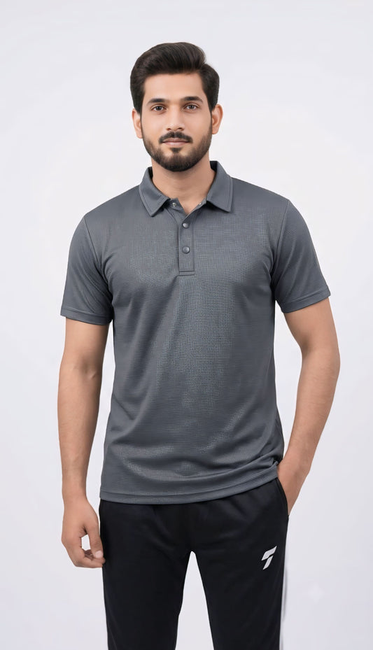 A man wearing a dark gray short-sleeve polo shirt and black track pants, standing against a light gray studio background.