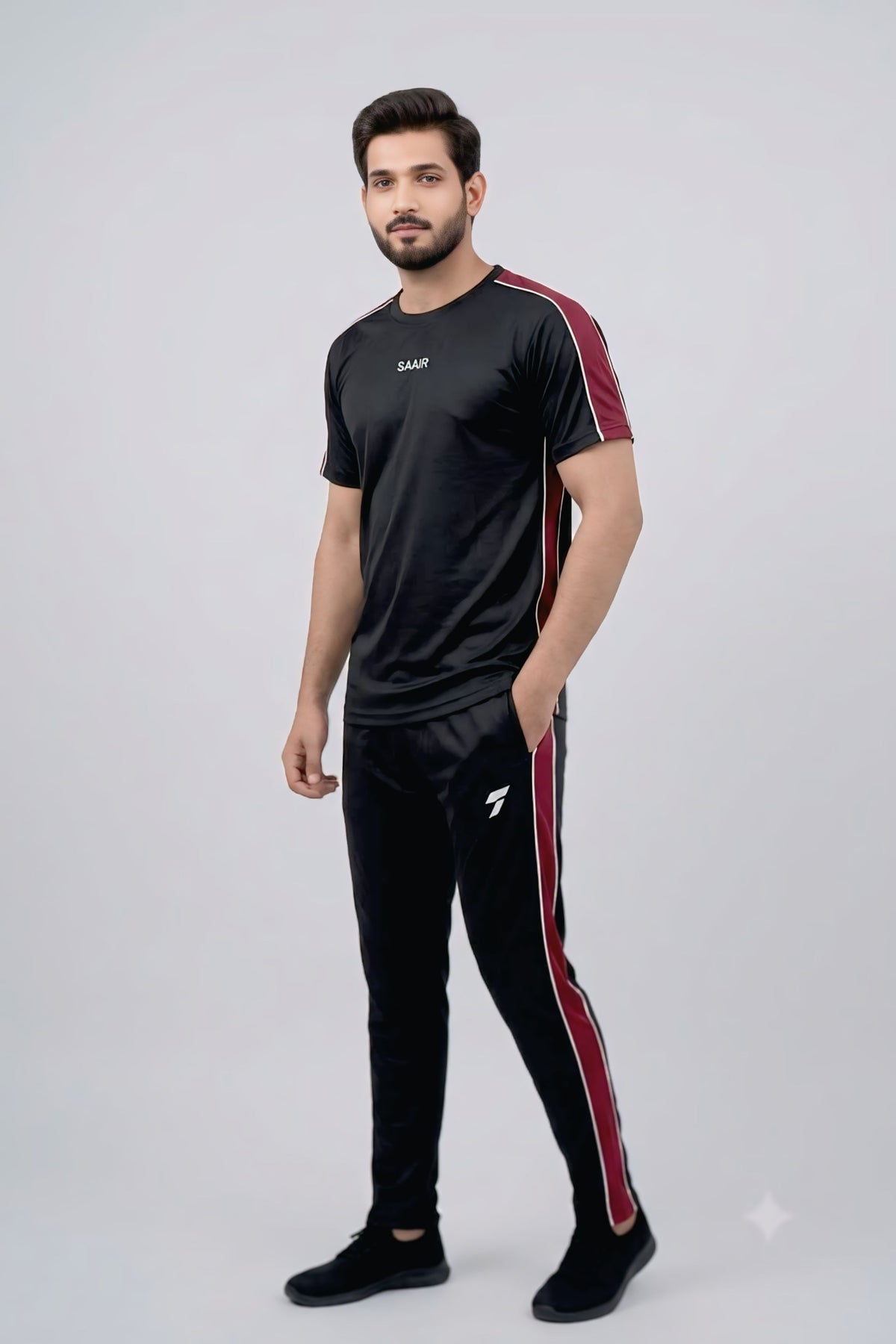 A man modeling a black athletic tracksuit with red side stripes, featuring a short-sleeve t-shirt and matching joggers, against a light gray studio background.