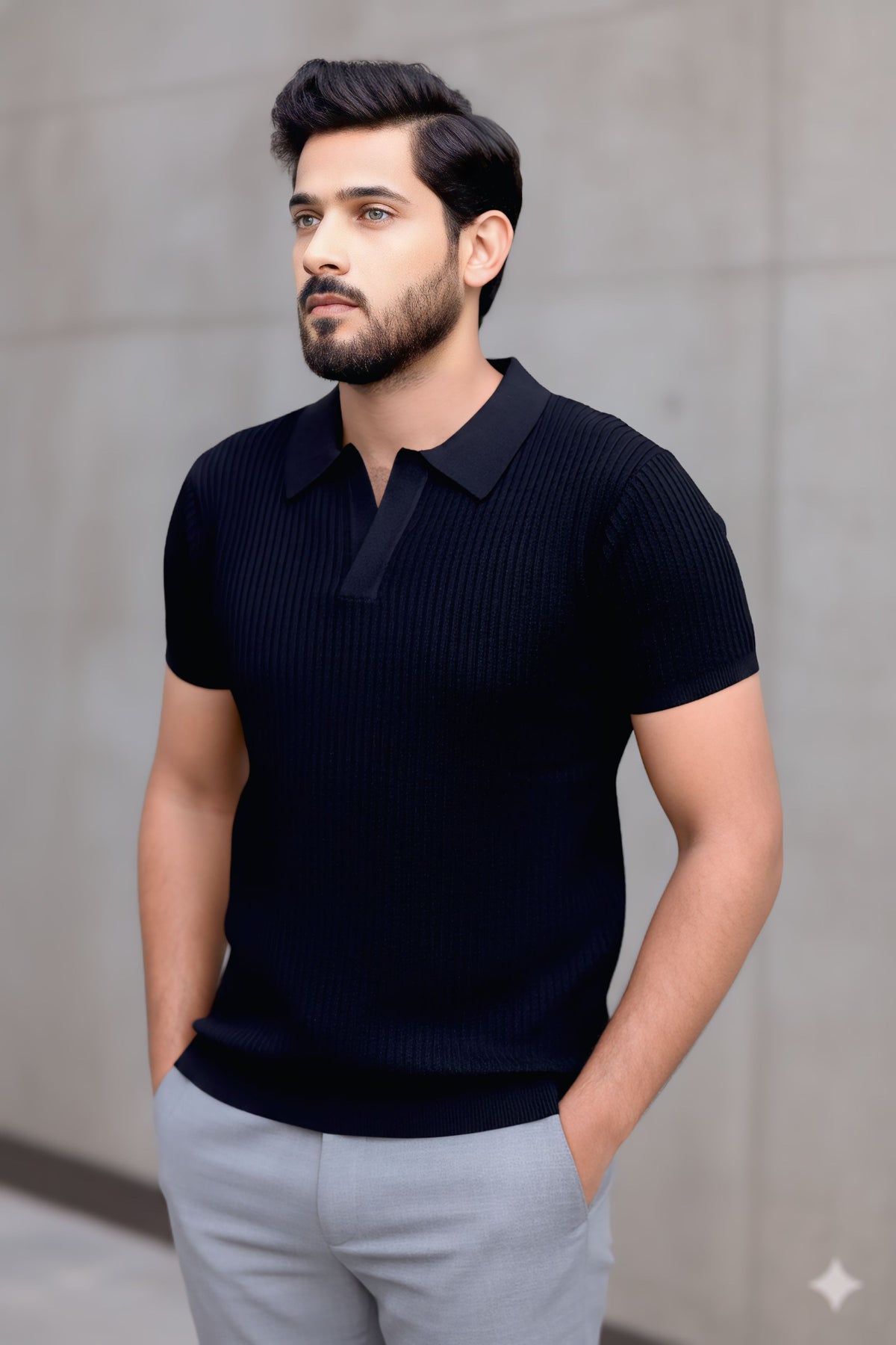 A man wearing a dark navy ribbed short-sleeve polo shirt and light gray trousers, standing against a neutral concrete wall.