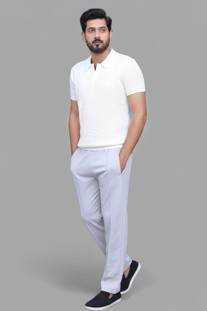 A man modeling a white short-sleeve polo shirt and light gray trousers, standing against a solid gray background.