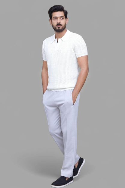 A man modeling a white short-sleeve polo shirt and light gray trousers, standing against a solid gray background.