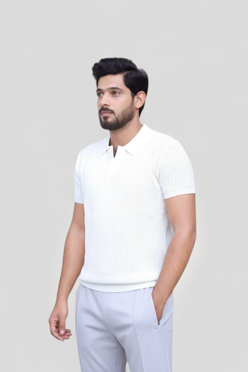 A man wearing a white short-sleeve ribbed knit polo shirt and light gray trousers, standing against a solid light gray background.